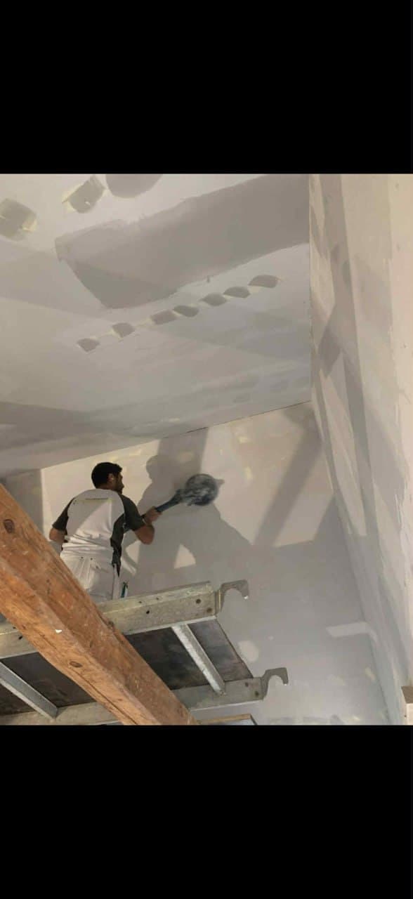 Maler spartler loft fra stillads i nybyggeri — professionelt spartlingsarbejde
